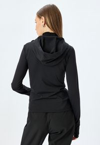 Zwarte hoodie met lange mouwen en een slim fit ontwerp, gemaakt van glad, rekbaar materiaal, met een hoge halslijn en een standaard capuchon.