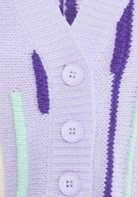 Pletený kardigán v levanduľovej farbe s vertikálnymi fialovými a mätozelenými vzormi. Má tri fialové gombíky a rebrovaný výstrih do V.