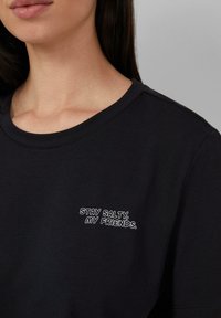 Czarna bawełniana koszulka z okrągłym dekoltem i krótkimi rękawami. Posiada białe haftowane napisy: "STAY SALTY, MY FRIENDS." w pobliżu ramienia.