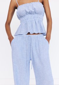 Lichtblauw en wit gestreepte peplumtop met elastische taille, gecombineerd met bijpassende losse broek met trekkoord en zijzakken.