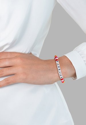 Bunter Perlenarmband mit weißen Buchstaben, die "FOREVER" buchstabieren, mit roten, pinken und gelben Perlen. Am Handgelenk getragen, zusammen mit einem weißen Hemd.