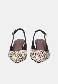 Un par de zapatos de punta afilada con tira trasera, en estampado animal beige y negro con ribete negro, exhibidos sobre un fondo blanco.