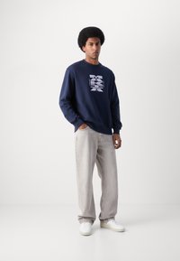Sudadera navy con logo gráfico blanco, combinada con jeans sueltos de color gris claro y zapatillas blancas. Tela suave, corte relajado, diseño minimalista.