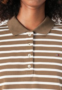 Brun og hvit stripete polo skjorte med krage og tre knapper. Har en liten logo i hjørnet. Laget av bomull.