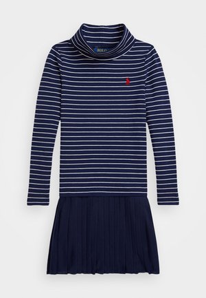 Ναυτικό μπλε φόρεμα με ρίγες, αρκετά ψηλό λαιμό, μακριά μανίκια και πλισέ φούστα. Διαθέτει αντίθετες λευκές ρίγες και κόκκινο λογότυπο στο στήθος.