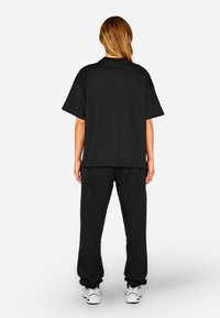Schwarzes Baumwoll-T-Shirt mit kurzen Ärmeln und lockerer Passform, kombiniert mit passenden schwarzen Sweatpants. Modell trägt weiße Turnschuhe.