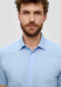 Helles blaues Kurzarmhemd mit spitzem Kragen, ausgestattet mit einer geknöpften Front und glattem, dezent strukturiertem Stoff.