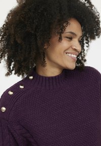 Pull en tricot violet avec un col côtelé, décoré de trois boutons dorés sur l'épaule gauche et d'un tissu texturé.