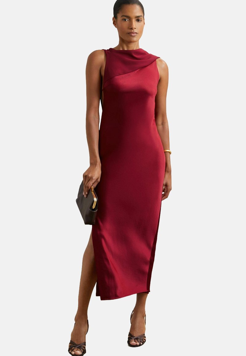 Burgunderfarbendes Satinkleid mit drapiertem Ausschnitt, seitlichem Schlitz und figurbetontem Design. Kombiniert mit einer schwarzen Clutch und Riemchenabsätzen.