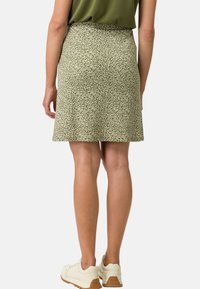 Jupe verte à motifs avec un design évasé, ornée d'un imprimé en forme de feuilles blanches et d'une texture lisse ; associée à des chaussures de couleur claire.