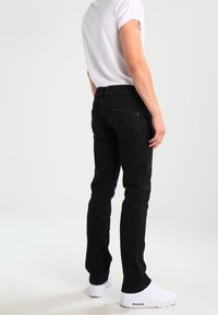 Schwarze Jeans aus Denim mit schlanker Passform, Five-Pocket-Design, typischer Nahtführung und leicht elastischem Material. Kombiniert mit einem weißen T-Shirt mit kurzen Ärmeln.