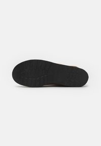 Suela de zapato negra con patrones texturizados, que presenta surcos definidos y un diseño robusto para ofrecer tracción y durabilidad.