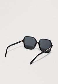 Čierne slnečné okuliare s obdĺžnikovými rámami, tmavými sklami a úzkymi ramenami, otvorené a položené na svetlom, neutrálnom pozadí.
