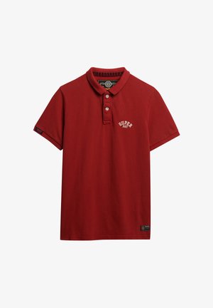 Czerwona koszulka polo z krótkimi rękawami, zapinana na guziki, z wyszywanym logo "SUPER DRY" na piersi oraz tkana metka na dole.