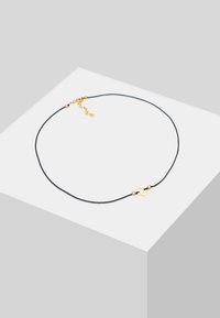 Black cord necklace with a gold-tone metal accent featuring a floral shape and small round beads, adjustable with a chain extension.