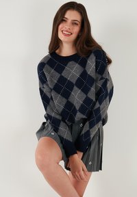 Navy and gray argyle-patterned sweater in a soft material, featuring a round neckline and long sleeves, paired with a pleated gray skirt.