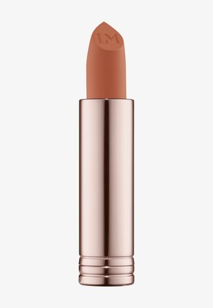 Læbestift i et metallic rosaguld rør, med en afrundet spids præget med "LM." Farven er en varm nude tone med en glat tekstur.