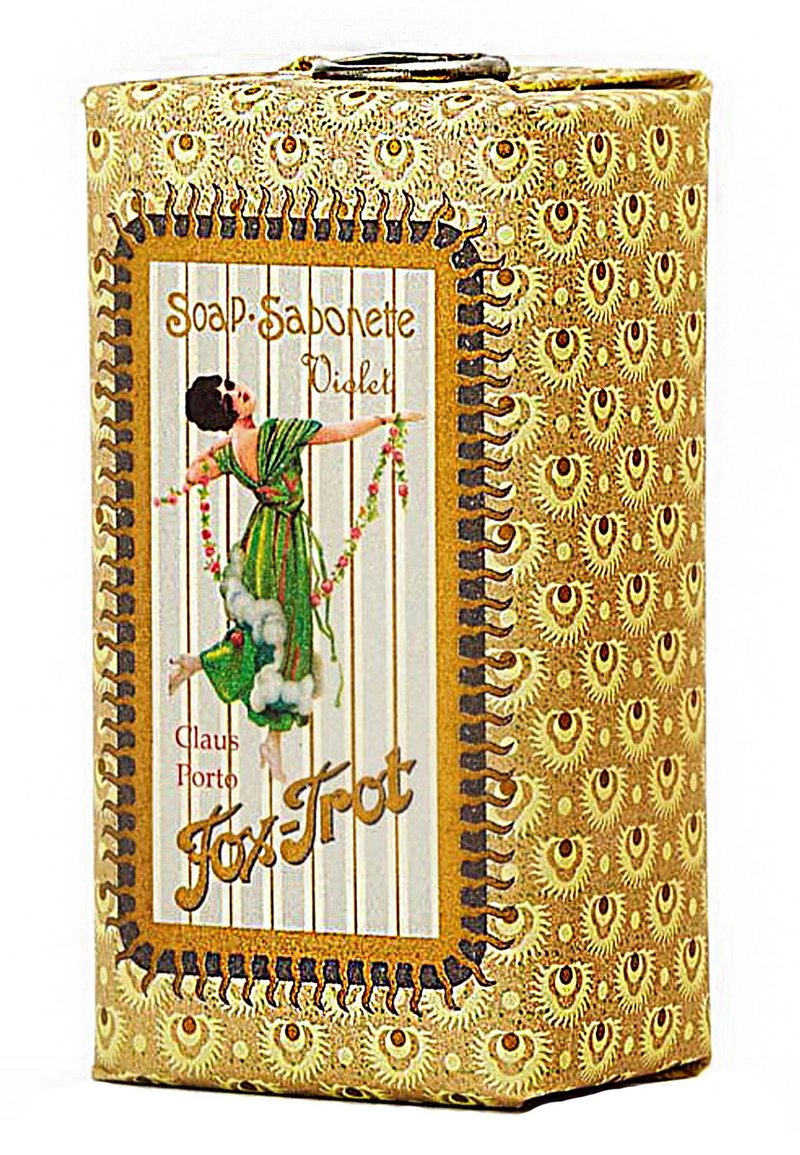 Violette Seifenverpackung mit einem dekorativen gold- und braunfarbenen Muster. Enthält eine Darstellung einer Figur in Grün, die Blumen hält und von Wolken umgeben ist.