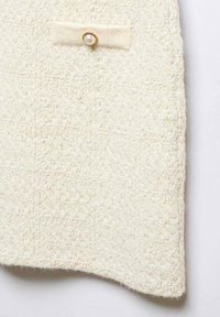 Tissu texturé couleur crème avec un petit nœud et un bouton en perle près du centre supérieur.