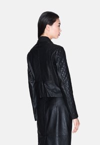 Giacca nera in pelle cropped con maniche trapuntate e texture del corpo liscia. Presenta un colletto e un design aderente, che mette in mostra la lavorazione di alta sartoria.