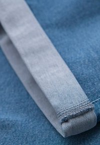 Zbliżenie na niebieski materiał dżinsowy z starannie złożonym jasnoniebieskim mankietem, ukazujące szczegółowe szwy i fakturę.
