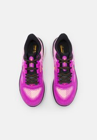 Pár růžových a černých běžeckých bot s černými tkaničkami a oranžovými logy Nike, z pohledu shora na bílém pozadí.