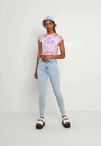 Rosa tie-dye crop topp med blomstermønster, lyseblå skinny jeans og hvite sandaler med svarte såler. Blå bøttehatt.