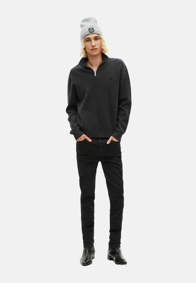 Zwarte half-zip pullover trui met lange mouwen, zachte textuur, gedragen met zwarte jeans en een grijze beanie met een ronde logo.