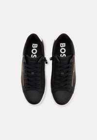 Paire de baskets basses noires avec lacets noirs, fermeture éclair latérale, détail de bande marron et semelles blanches, vues de dessus.