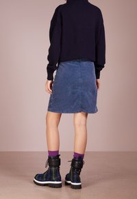 Marineblauer Strickpullover, Jeansrock in Blau und schwarze karierte Ankle Boots mit weißen Sohlen sowie lila Socken. Fokus auf einen bequemen, lässigen Stil.