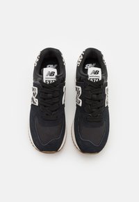 Sneaker nere con tomaia in suede e mesh, caratterizzate da un tallone con motivo, lacci neri e logo New Balance bianco sulla linguetta e sul lato.