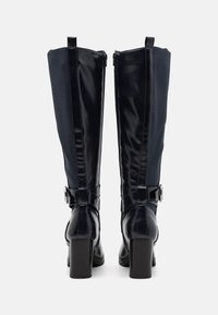 Botas hasta la rodilla con un diseño elegante, material brillante en color navy, cremalleras laterales y tacones de bloque rectangulares con acentos de hebilla plateada.