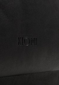 Svart fusk läderväska med präglad "KIOMI"-logotyp. Slät textur med subtil kornighet och minimalistisk design.