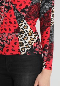 Langärmliges Oberteil mit einem Patchwork-Design aus roten, schwarzen und Tierfellmustern. Weiches, dehnbares Material mit unterschiedlichen Texturen.