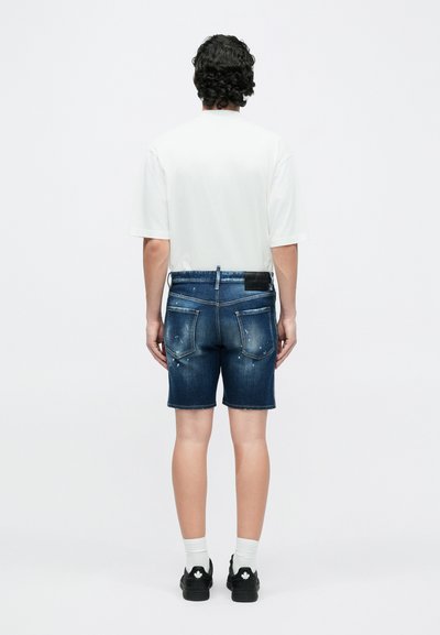 Short en denim délavé, avec cinq poches et des passants pour ceinture, accompagné d'un t-shirt blanc à manches courtes et de chaussures noires.