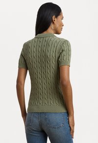Pull en maille vert olive à manches courtes avec motif en relief, col et ourlet côtelés, associé à un jean en denim bleu ajusté.