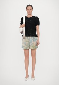 Zwarte textuur top met pofmouwen, gecombineerd met lichte shorts met een groene loofprint. Accessoire: kleine witte handtas. Witte hakken.