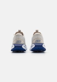 Nike sneakers med en lys grå mesh-overdel, hvid mellemsål, blå ydersål og en fremtrædende blå logo på hælen.