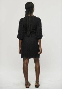 Black lace dress with three-quarter puff sleeves, fitted bodice, and a flared skirt. Smooth texture and intricate lace pattern detail.