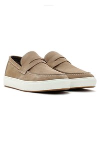 Mocasines de gamuza marrón con una suela de goma blanca, que presentan un diseño cosido en la parte superior y una textura suave.