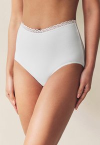 Weiße hochgeschnittene Unterwäsche mit einem strukturierten Spitzenbesatz entlang des Taillenbands und glattem Stoff. Verfügt über eine klassische Slipsilhouette.