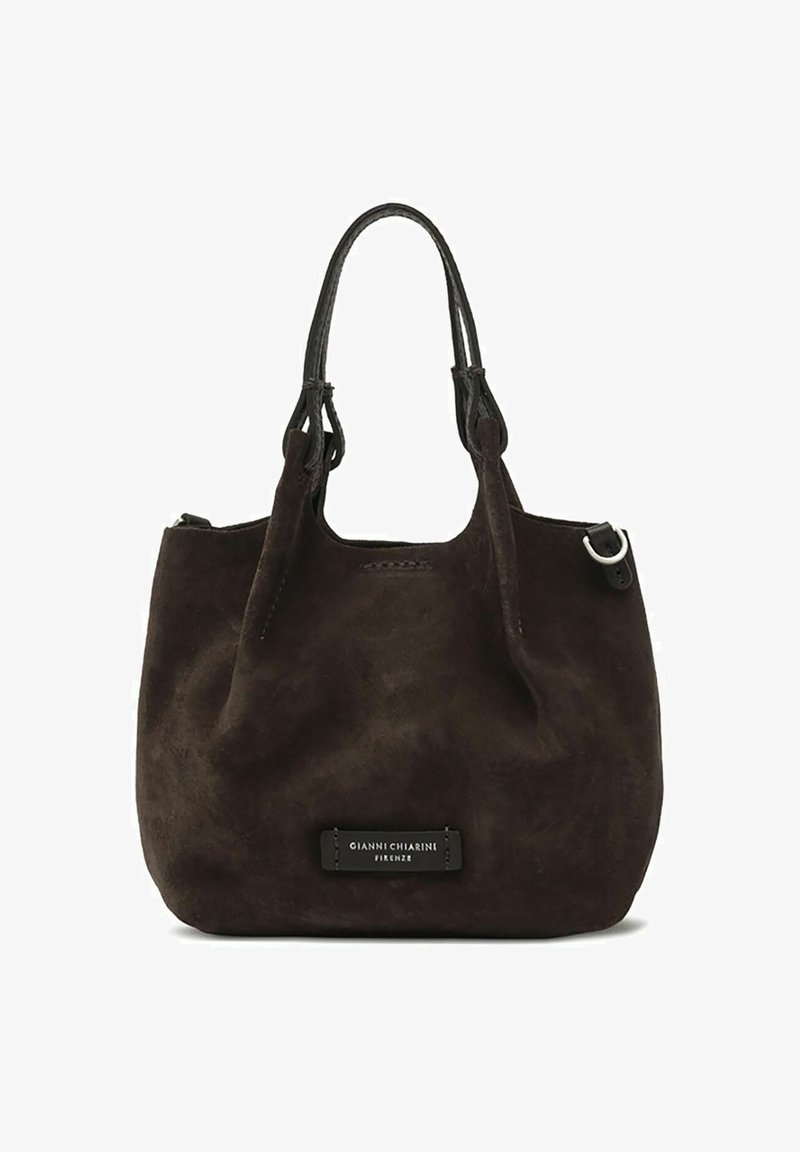 Bolso de ante marrón oscuro con dos asas de cuero, acentos de hardware plateado y un parche con el logotipo en la parte frontal. Textura suave y forma redondeada.