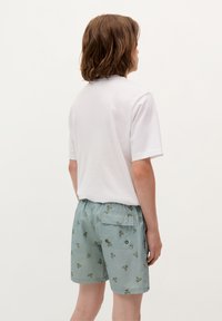 T-shirt bianca a maniche corte abbinata a pantaloncini azzurri chiari con un motivo di teschi verdi e una tasca posteriore con chiusura a pulsante.