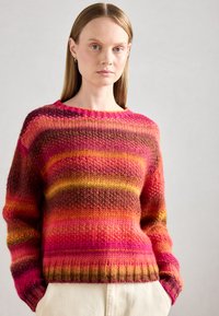 Multikleurige gebreide trui met levendige roze, oranje en bruine strepen, met een ronde halslijn en ribgebreide manchetten, gemaakt van zachte wol.