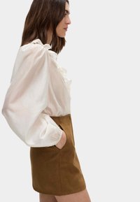 Witte blouse met pofmouwen en een gerimpelde halslijn, gecombineerd met een bruine suède minirok met zijzakken en een aansluitend ontwerp.