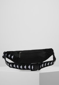 Czarna torba na spodniach z materiału z zamkiem błyskawicznym. Regulowany pasek z powtarzającym się wzorem białego logo. Gładka tekstura, prostokątny kształt.