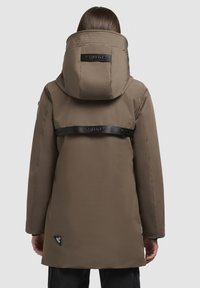 Hnedá zateplená parka s veľkou, hrejivou kapucňou, čiernymi popruhmi na zadnej strane a logom na dolnej časti. Hladká textúra.