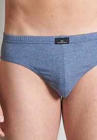 Culotte en coton gris-bleu avec une ceinture douce et une petite étiquette de marque. Le tissu a une texture lisse et un design ajusté.