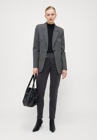 Grå mønstrete blazer, svart polohette, mørkegrå cordbukser, svart patent totebag og spisse svarte ankelstøvler.