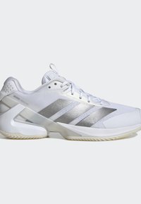 Wit en zilver laaggesneden Adidas Adizero Ubersonic tennisschoen met veters aan de voorkant en een getextureerde zool, zijaanzicht op een grijze achtergrond.